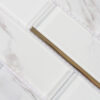 White Marble Glass Subway Tile In Staggered Pattern With Slim Gold Line Accents